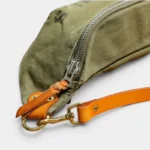 Sac Banane Toile Kaki Militaire Bandoulière Cuir Véritable Sac banane en toile kaki militaire, gros plan sur la fermeture éclair argentée avec mousqueton et bandoulière en cuir cognac