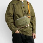 Sac Banane Toile Kaki Militaire Bandoulière Cuir Véritable Sac banane toile kaki militaire porté en bandoulière par un homme au style workwear, avec sangle en cuir orange