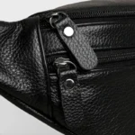 Sac Banane Homme Cuir Grainé Demi-Lune Sac banane homme en cuir grainé noir, gros plan sur les zips et anneaux métalliques argentés