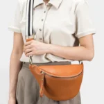 Sac Banane Femme Cuir Grainé Demi-Lune Chic Sac banane en cuir grainé camel porté en bandoulière par une femme au style chic et élégant, vue de face