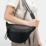 Sac Banane Femme Cuir Grainé Demi-Lune Chic Sac banane en cuir grainé noir porté en bandoulière par une femme au style chic et élégant