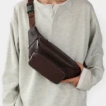 Sac Banane Homme Cuir Grainé Minimaliste Sac banane en cuir grainé marron porté en bandoulière par un homme, de face au style casual chic