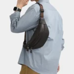 Sac banane homme en cuir grainé marron foncé, porté en bandoulière dans le dos par un homme au style classique-décontracté