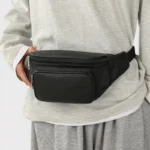 Sac Banane Homme Cuir Grainé Minimaliste Sac banane en cuir grainé noir porté à la taille de face par un homme au style streetwear