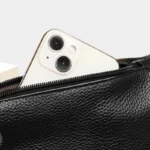 Sac Banane Homme Cuir Grainé Demi-Lune Sac banane en cuir grainé noir, gros plan sur la poche avant ouverte avec un iPhone glissé à l'intérieur