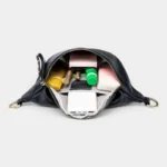 Sac Banane Femme Cuir Grainé Demi-Lune Chic Sac banane en cuir grainé noir vu de dessus, poche principale ouverte révélant une doublure chevronnée et des cosmétiques