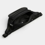 Sac Banane Homme Cuir Grainé Minimaliste Sac banane en cuir grainé noir posé à plat, poche principale ouverte révélant une poche zippée intérieure