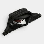 Sac Banane Homme Cuir Grainé Minimaliste Sac banane en cuir grainé noir vu de dessus, poche principale ouverte révélant un téléphone et un parapluie