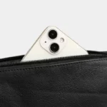 Sac Banane Homme Cuir Grainé Minimaliste Sac banane en cuir grainé noir, gros plan sur la poche zippée ouverte avec un smartphone glissé à l'intérieur
