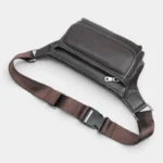 Sac banane cuir motard marron foncé posé de côté, sangle réglable déployée à l'avant du sac