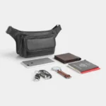 Sac banane cuir motard poche rabat noir posé aux côtés de tous les essentiels qu'il peut contenir