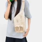 Grand sac banane femme en nylon beige porté en bandoulière croisée par une femme au style coréen casual-chic, vu de face