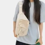 Sac banane femme en nylon beige porté en bandoulière croisée par une femme, de face au style streetwear