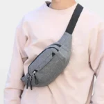 Sac banane en nylon gris porté en bandoulière par une personne au style streetwear décontracté, vue de face
