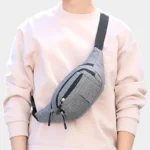 Sac banane en nylon gris chiné porté en bandoulière croisée par une femme au style streetwear décontracté