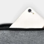 Sac banane gris en nylon, gros plan sur la poche zippée ouverte avec un smartphone
