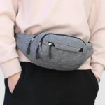 Sac banane nylon gris porté à la taille de face, avec plusieurs poches zippées apparentes