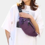 Sac banane en nylon violet porté en bandoulière par une femme au style streetwear décontracté, vue de face