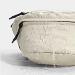 Sac banane en nylon froissé beige, gros plan de face avec des gouttes d'eau ruisselant sur la surface