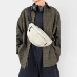 Sac banane nylon froissé beige porté en bandoulière par un homme de face au style workwear