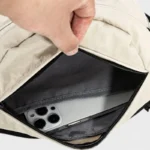 Sac banane nylon beige, gros plan sur la poche avant ouverte révélant un smartphone
