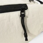 Sac banane nylon froissé beige, gros plan sur la tirette de corde noire de la fermeture éclair