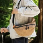 Grand Sac Banane Nylon Ripstop Quadrillé Imperméable Sac banane nylon quadrillé orange porté en bandoulière par un randonneur, de profil en forêt