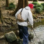 Grand Sac Banane Nylon Ripstop Quadrillé Imperméable Sac banane nylon quadrillé beige porté en bandoulière dos par un homme, de dos lors d'une randonnée en forêt