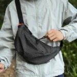 Grand Sac Banane Nylon Ripstop Quadrillé Imperméable Sac banane nylon quadrillé noir porté en bandoulière de face par un randonneur au style outdoor