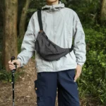 Grand Sac Banane Nylon Ripstop Quadrillé Imperméable Sac banane nylon quadrillé noir porté en bandoulière par un homme de face lors d'une randonnée en forêt