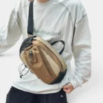 Sac banane randonnée en nylon ripstop beige porté en bandoulière de face par un homme au style streetwear