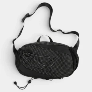 Sac banane randonnée en nylon noir quadrillé, posé à plat avec une sangle à clip plastique