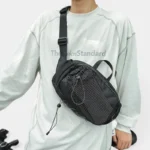Grand sac banane randonnée en nylon noir porté en bandoulière par un homme au style streetwear