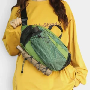 Grand sac banane randonnée porte-gourde en nylon vert porté en bandoulière par une femme au style streetwear