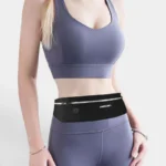 Sac Banane Running Ultra Fin Imperméable Réfléchissant Sac banane running noir en nylon porté à la taille par une femme, de face au style sportif