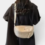 Grand Sac Banane Femme Velours Côtelé Demi-Lune Sac banane en velours côtelé beige porté en bandoulière dans le dos par une femme au style chic-casual
