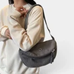 Grand Sac Banane Femme Velours Côtelé Demi-Lune Sac banane en velours côtelé gris porté en bandoulière par une femme au style casual-chic, vue de face