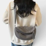 Grand Sac Banane Femme Velours Côtelé Demi-Lune Sac banane en velours côtelé gris porté dans le dos par une femme, vue de dos au style casual-chic
