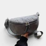 Grand Sac Banane Femme Velours Côtelé Demi-Lune Sac banane velours côtelé demi-lune gris tenu à la main, présenté de face avec sa sangle réglable assortie