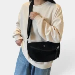 Grand Sac Banane Femme Velours Côtelé Demi-Lune Sac banane velours côtelé demi-lune noir porté en bandoulière par une femme au style casual-chic