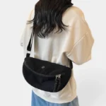 Grand Sac Banane Femme Velours Côtelé Demi-Lune Sac banane en velours côtelé noir porté en bandoulière dans le dos par une femme au style casual-chic
