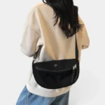 Grand Sac Banane Femme Velours Côtelé Demi-Lune Sac banane en velours côtelé noir porté en bandoulière de dos par une femme au style casual-chic