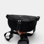 Grand Sac Banane Femme Velours Côtelé Demi-Lune Sac banane en velours côtelé noir tenu à la main, présenté de face avec sa sangle réglable