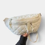 Grand Sac Banane Femme Velours Côtelé Matelassé Grand sac banane en velours côtelé matelassé beige, tenu à la main de face avec sa sangle crème