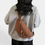 Grand Sac Banane Femme Velours Côtelé Matelassé Grand sac banane en velours côtelé matelassé camel, porté en bandoulière dans le dos par une femme au style casual-chic