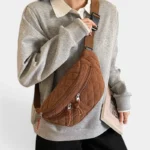 Grand Sac Banane Femme Velours Côtelé Matelassé Grand sac banane en velours côtelé caramel porté en bandoulière croisée par une femme au style décontracté-chic, de face