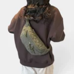 Grand Sac Banane Femme Velours Côtelé Matelassé Sac banane en velours côtelé matelassé vert kaki porté en bandoulière dans le dos par une femme au style casual-chic