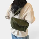 Grand Sac Banane Femme Velours Côtelé Demi-Lune Sac banane en velours côtelé vert kaki porté en bandoulière croisée par une femme au style casual-chic, vu de dos