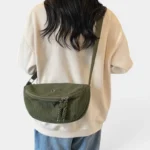 Grand Sac Banane Femme Velours Côtelé Demi-Lune Sac banane en velours côtelé vert kaki porté en bandoulière dans le dos par une femme au style casual-chic