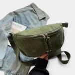 Grand Sac Banane Femme Velours Côtelé Demi-Lune Sac banane en velours côtelé vert kaki, posé de face, tenu par une main avec une sangle assortie